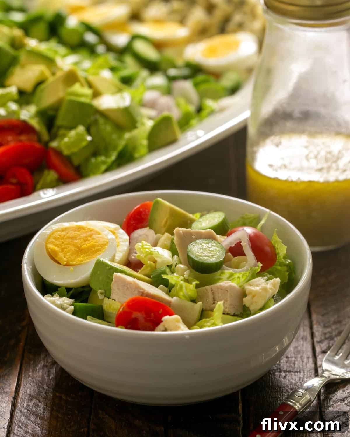 A beautifully arranged Cobb Salad bowl with the salad dressing in a jar and serving tray in the background.