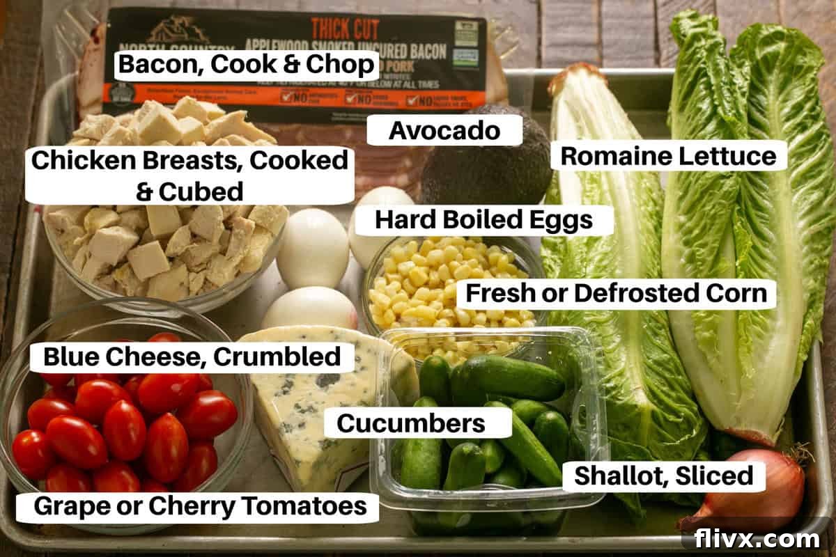 Various Cobb Salad ingredients, neatly arranged with labels, on a metal sheet pan for easy viewing and prep.