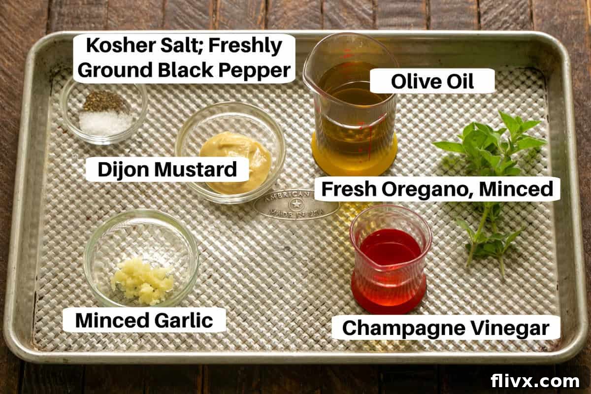 Cobb Salad Dressing Ingredients, including olive oil, champagne vinegar, Dijon mustard, fresh oregano, and garlic, displayed on a metal sheet pan.
