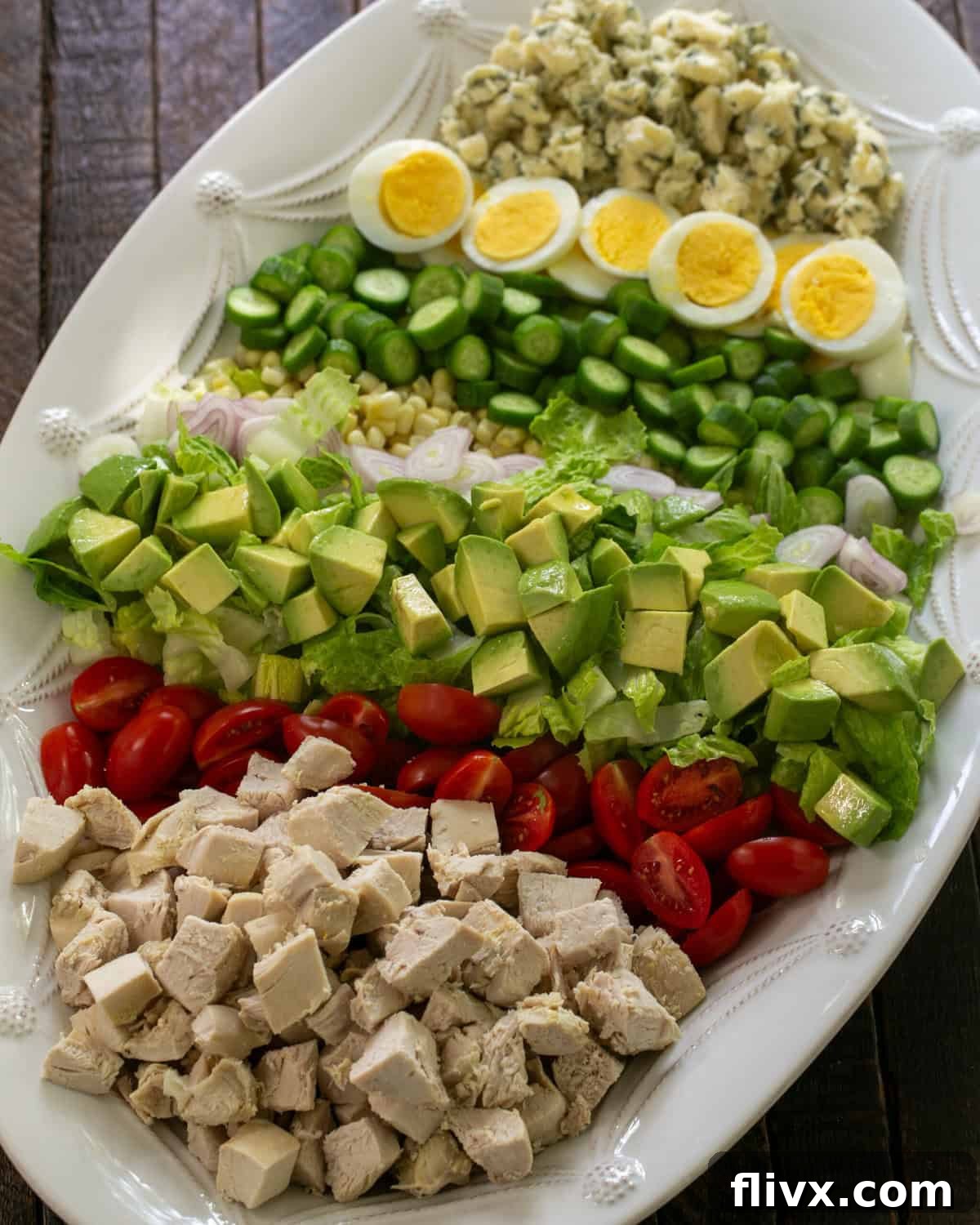 An overhead view of a perfectly composed Cobb salad, showcasing all the vibrant ingredients arranged in neat rows on a white serving platter.