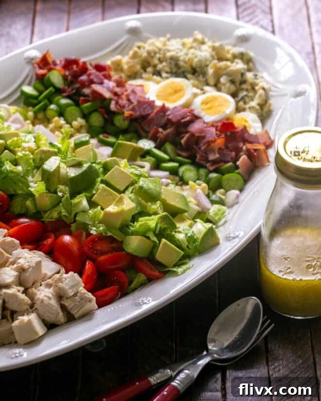 Prepared Cobb Salad ingredients neatly arranged on a serving platter, with salad dressing in a jar nearby, ready for serving.