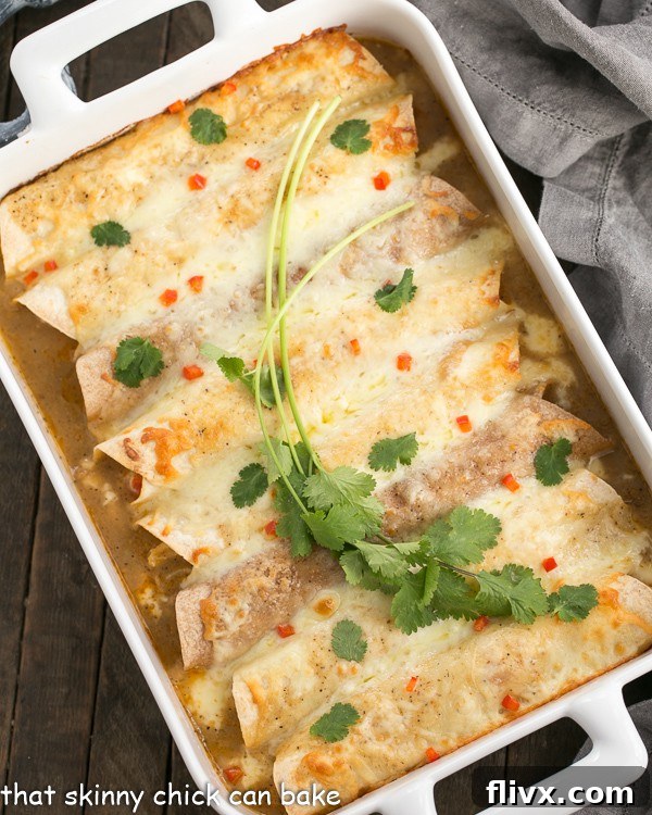 Overhead view of a white casserole dish filled with golden Cheesy Chicken Enchiladas, beautifully garnished with fresh cilantro.