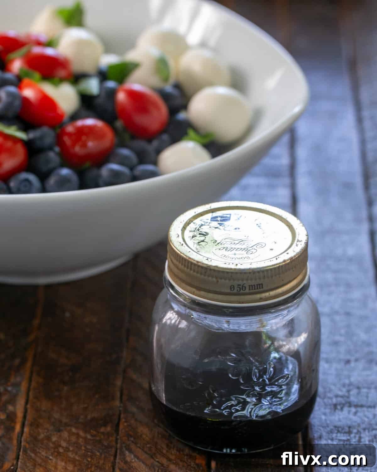 A vibrant Caprese Salad with Blueberries served in a white bowl, drizzled with Balsamic vinegar.