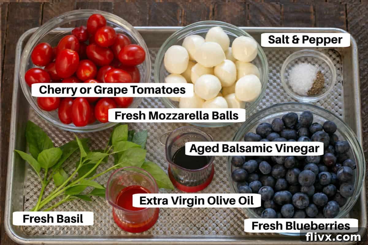 Various fresh ingredients for Blueberry Caprese Salad, including blueberries, tomatoes, mozzarella, and basil, arranged on a metal sheet pan with labels.