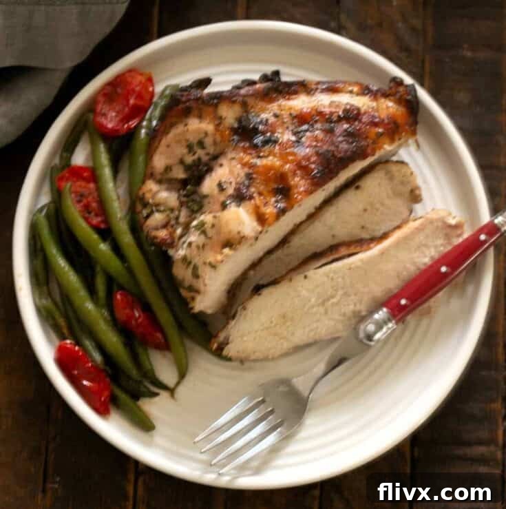 Overhead view of sliced chicken piccata on a white plate with a fork and green beans.