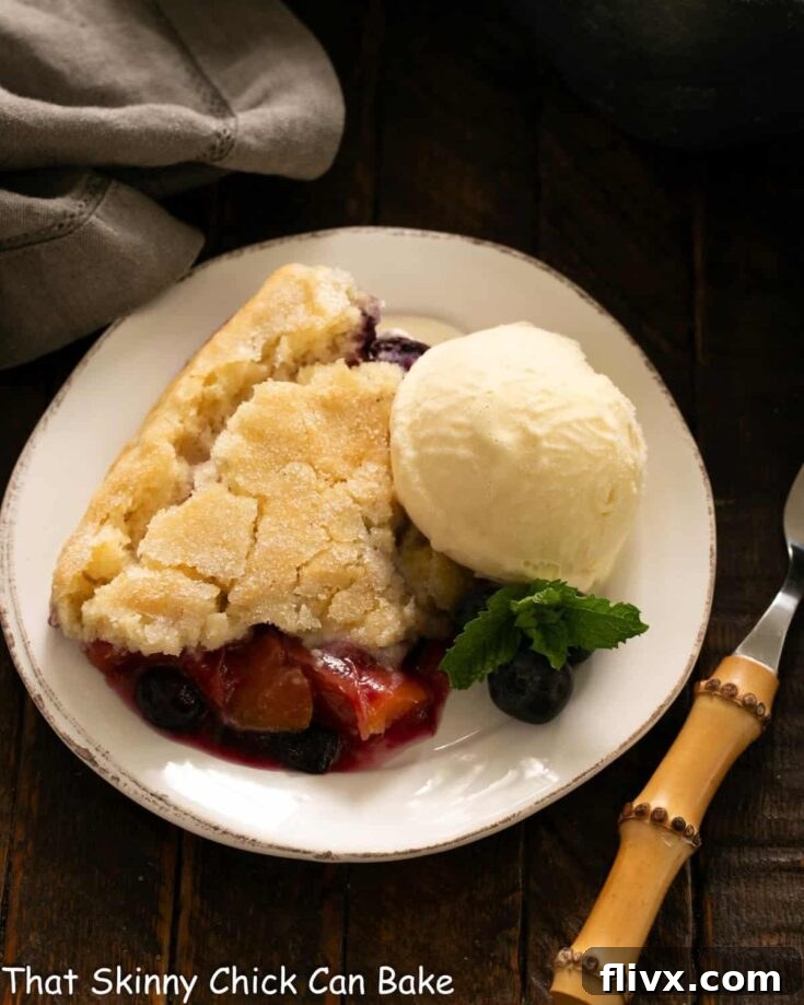 A warm Peach Blueberry Cobbler, bubbling with fruit and a golden biscuit topping, served in a dish.