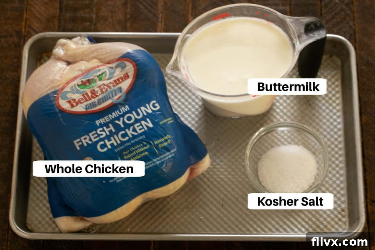 A simple array of buttermilk chicken ingredients, including a whole chicken, a carton of buttermilk, and a bowl of salt, thoughtfully arranged on a metal sheet pan.