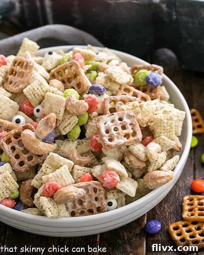Halloween Chex Mix in a white serving bowl, showcasing its diverse ingredients and tempting white chocolate coating.
