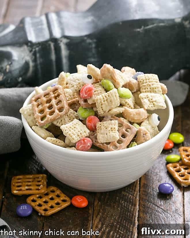 White bowl filled with white chocolate chex mix, garnished with Halloween candy eyeballs.