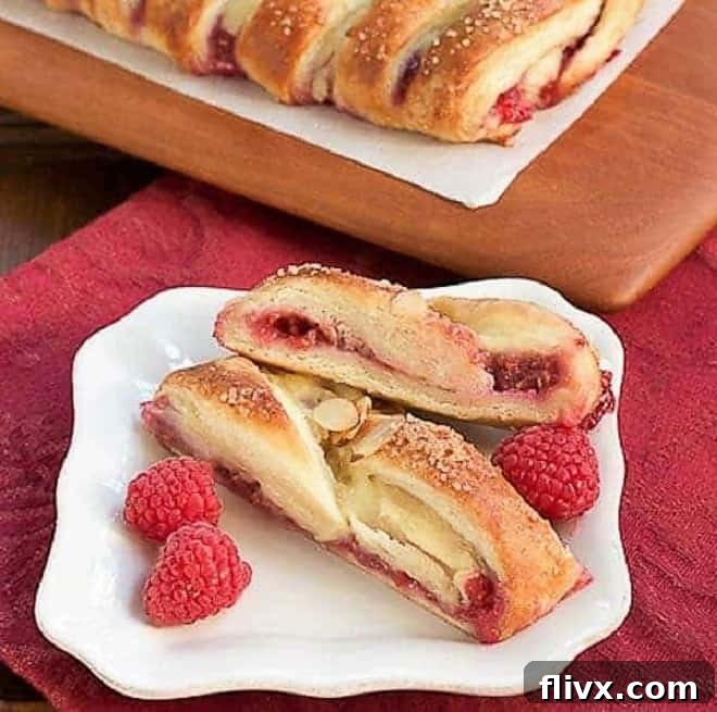 Raspberry Danish Pastry - Tender dough filled with raspberry and cream cheese. Plus how to make a cheater laminated dough! Tempting slices of Raspberry Danish Braid displayed on a pristine white ceramic plate, ready to be enjoyed.