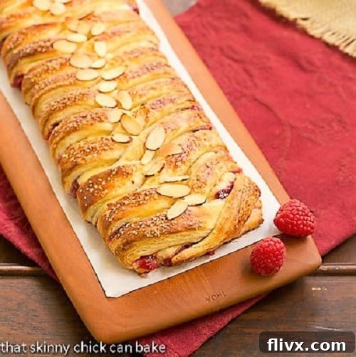 Homemade Raspberry Danish - Tender dough filled with raspberry and cream cheese. Plus how to make a cheater laminated dough! A beautifully baked Raspberry Danish Braid resting on a rustic wooden cutting board, showcasing its intricate pattern and golden crust.