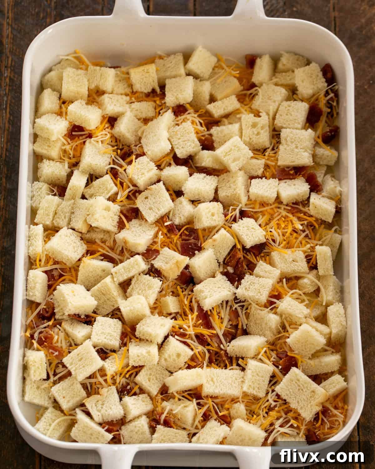 Bread cubes, bacon and cheese in the baking dish, lightly drizzled with butter.