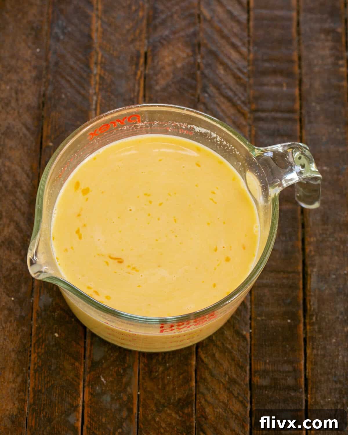 Beaten eggs, milk, dried mustard and salt are whisked together in a Pyrex measuring cup.