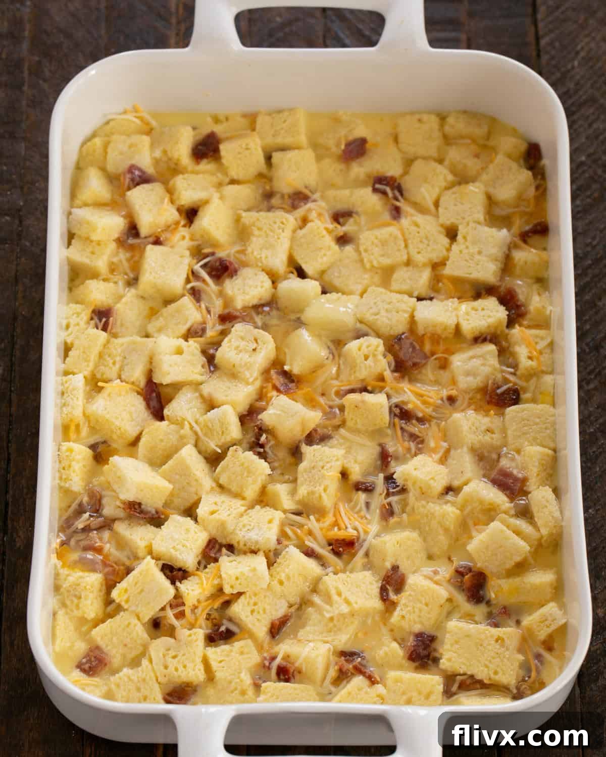 Cubed bread, bacon, and cheese in a baking dish covered with the egg custard mixture.