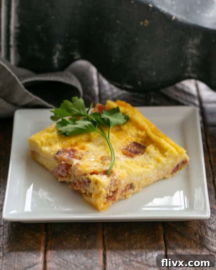 Slice of breakfast casserole on a white plate with a sprig of parsley.