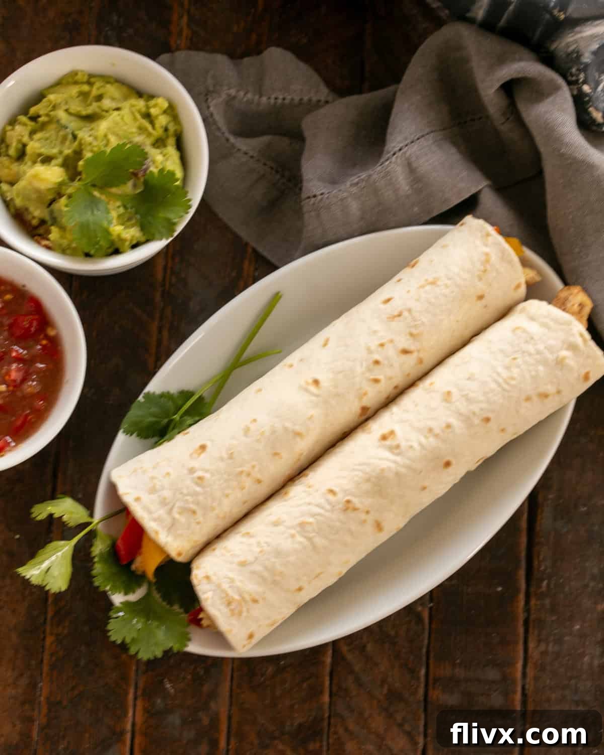 Overhead view of two chicken tortillas on a white plate with toppings to the side.