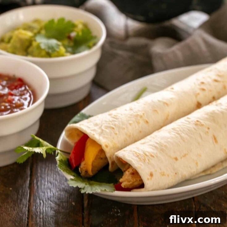 Two chicken fajitas on a white plate in front of bowls of guacamole and salsa.