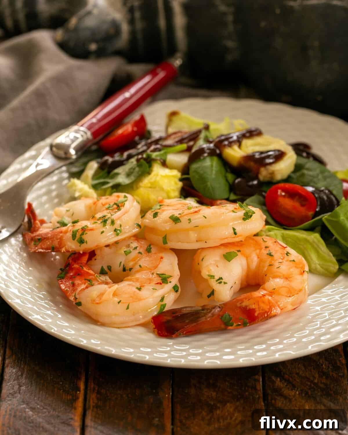Shrimp scampi on a white plate with salad and a red handled fork.