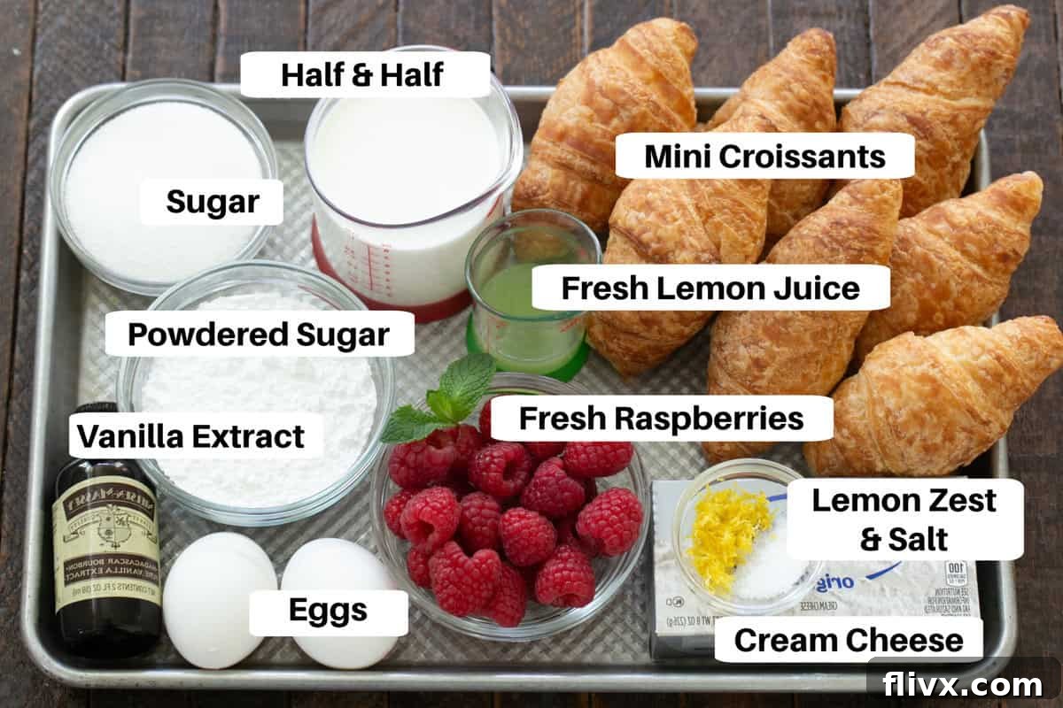 Fresh ingredients for Croissant French Toast including croissants, raspberries, eggs, half and half, cream cheese, and lemons, neatly arranged on a metal sheet pan.