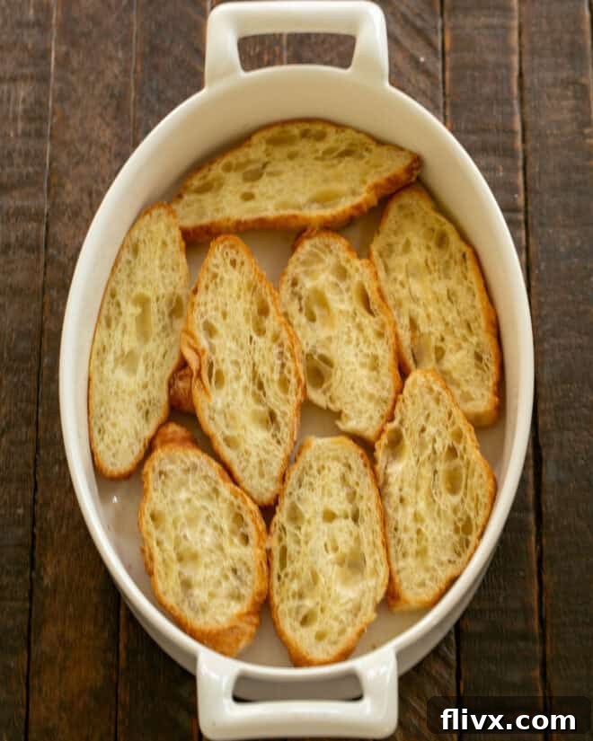 Mini croissants are sliced in half lengthwise and arranged cut-side up in a baking dish.