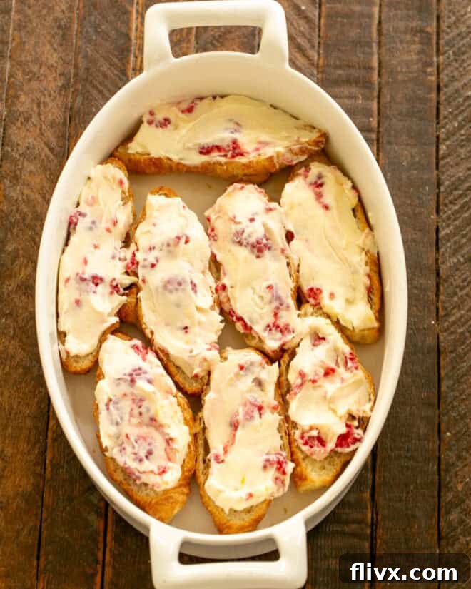 The raspberry cream cheese mixture is spread evenly over the cut croissant halves in a baking dish.