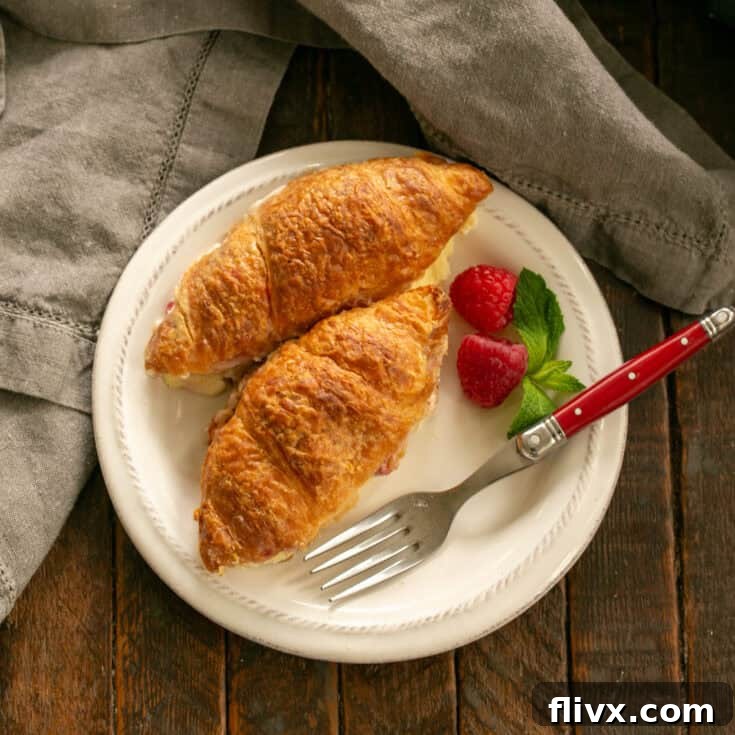 Overhead view of a beautiful Raspberry Croissant French Toast Casserole on a white plate, garnished with fresh berries and a light dusting of powdered sugar.