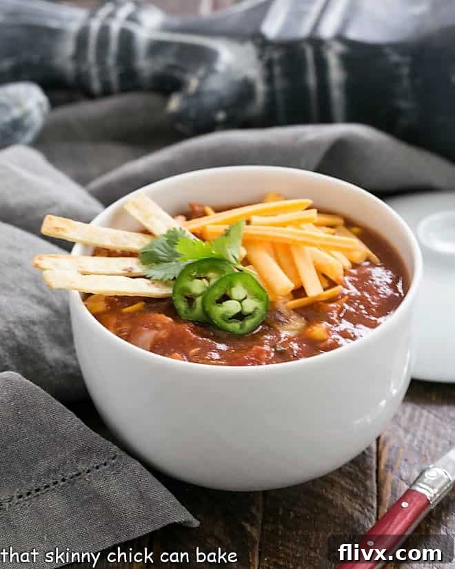 Side view of a white bowl filled with tortilla soup topped with garnishes.