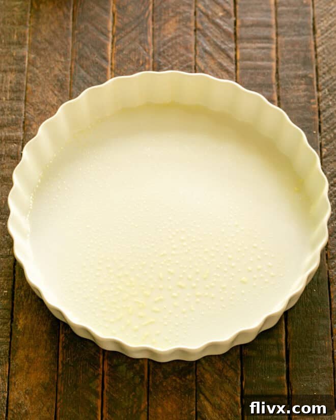 A round ceramic baking dish, buttered and ready for the raspberries, positioned on a countertop next to a preheated oven.