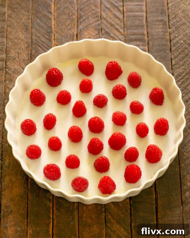 Fresh, vibrant red raspberries are carefully scattered in a single layer across the bottom of the prepared, buttered baking dish.