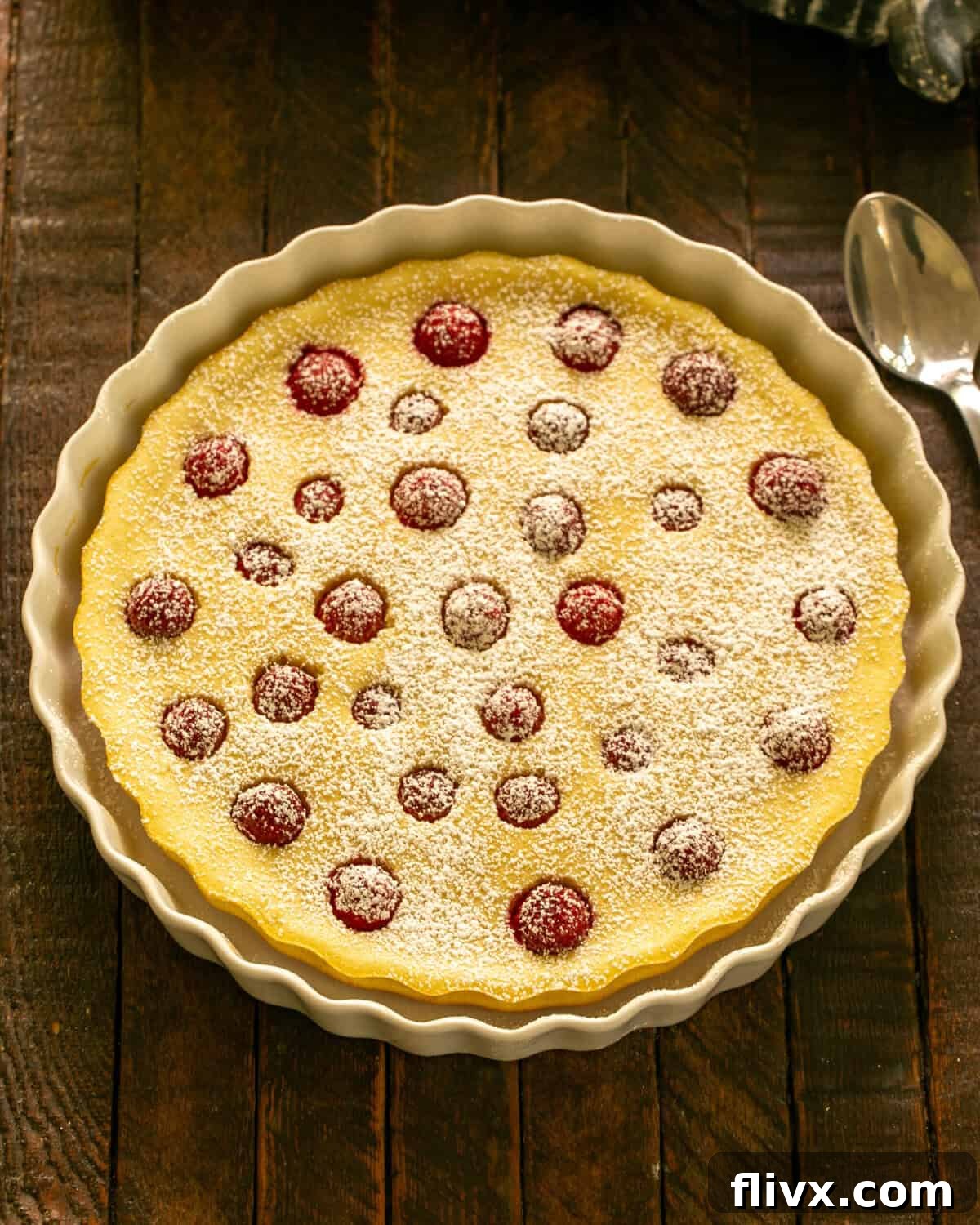 A fully baked Raspberry Clafoutis, cooled and dusted with powdered sugar, ready to be sliced into elegant wedges and served.