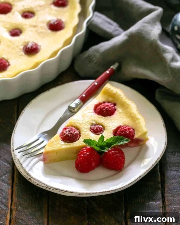 A perfectly portioned slice of Raspberry Clafoutis, beautifully presented on a pristine white plate, accompanied by a fork with a striking red handle.