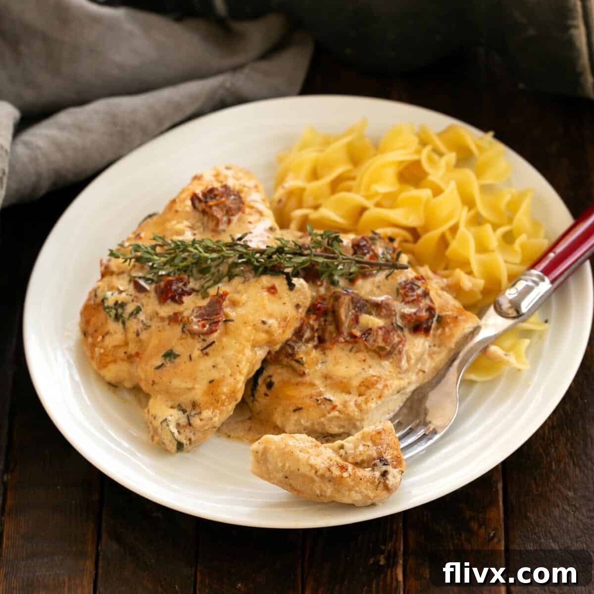 Two chicken breasts in a cream sauce topped with sprigs of thyme  served over egg noodles.