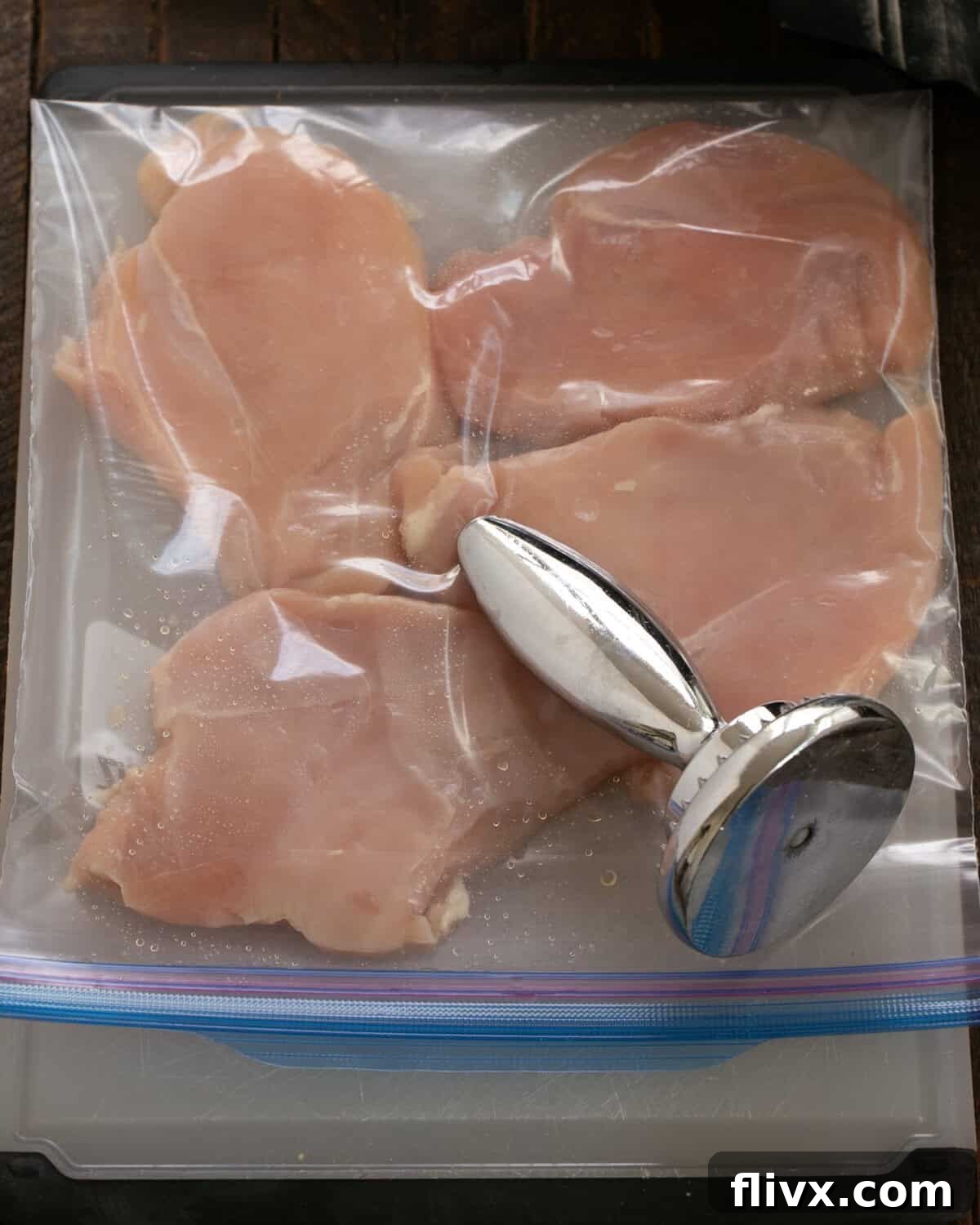 Boneless, skinless chicken breasts being pounded flat into cutlets with a meat mallet.