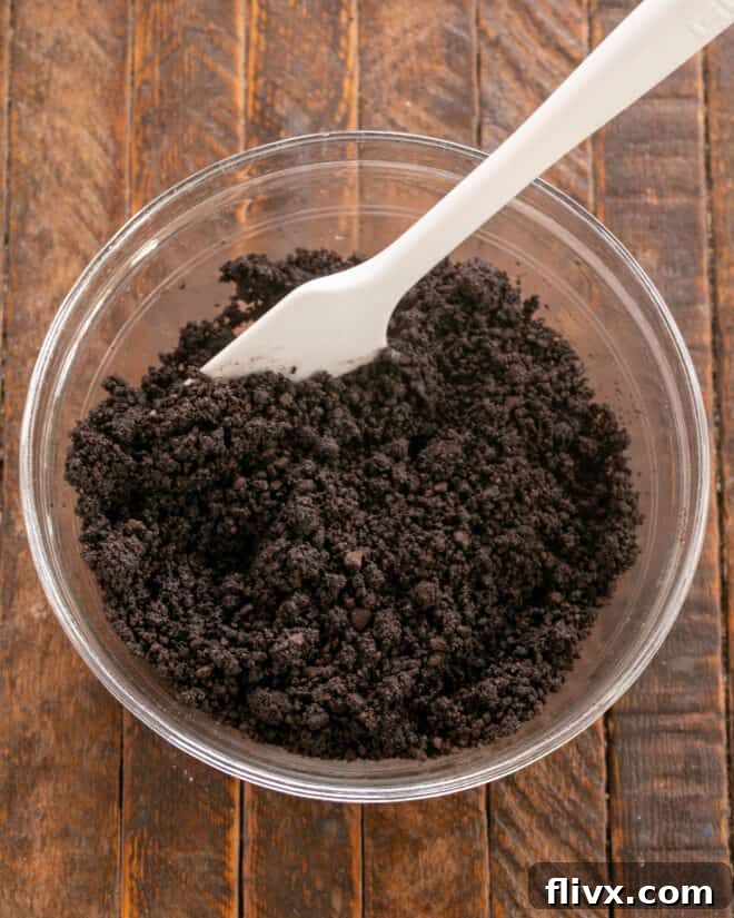 Cookie crumbs being mixed with melted butter and pressed into a prepared springform pan for the crust.