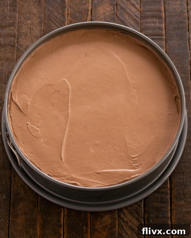 The prepared chocolate mousse filling being scraped into the cookie crust in the springform pan.