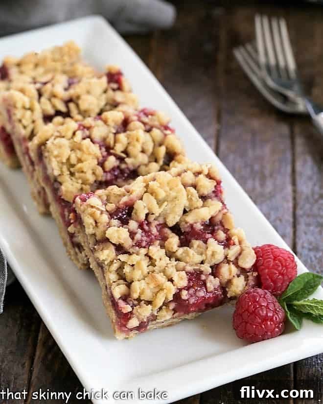 Freshly baked Raspberry Streusel Bars on a pristine white serving tray, showcasing their golden crumb topping and vibrant berry filling.