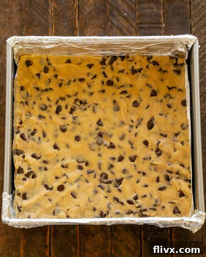 Half of the chocolate chip cookie dough pressed evenly into the bottom of a prepared baking pan lined with non-stick foil.