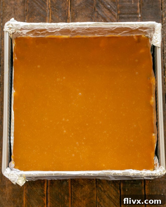 Melted caramel sauce being carefully poured over the first layer of cookie dough in the baking pan.