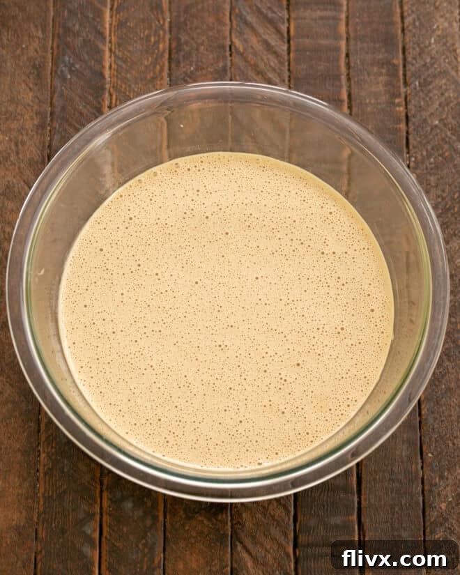 The egg, sugar, coffee, and vanilla mixture is being vigorously beaten in a stand mixer, transforming into a light, thick, and ribbon-like consistency after 10 minutes of whipping.