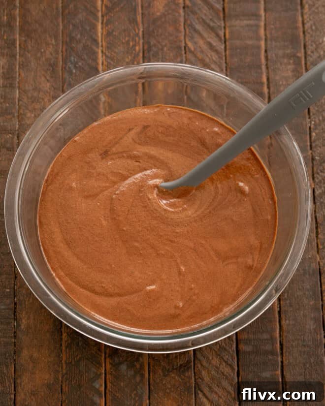 The melted chocolate mixture is slowly being incorporated into the whipped egg mixture in a stand mixer, creating a rich, uniform, and luxurious base for the double chocolate cookie dough.