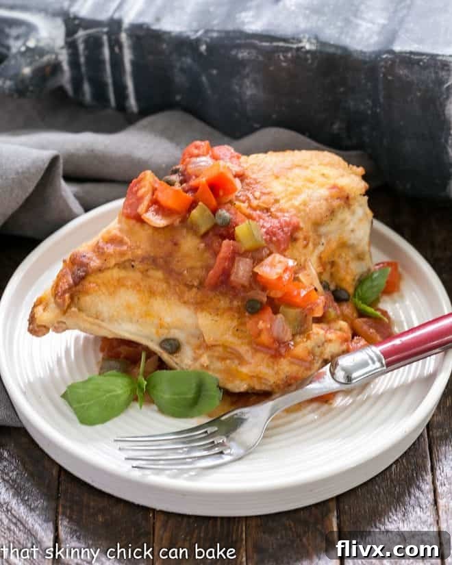 A perfectly cooked Chicken Cacciatore serving on a pristine white plate, accompanied by a fork with a striking red handle, highlighting the rich colors of the sauce and tender chicken.