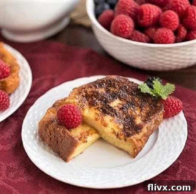 Sugar-Crusted French Toast Recipe - a double coating of sugar make this rich, eggy French toast dessert worthy! Sugar-Crusted French Toast Recipe cut in half and garnished with berries and mint on a white plate.