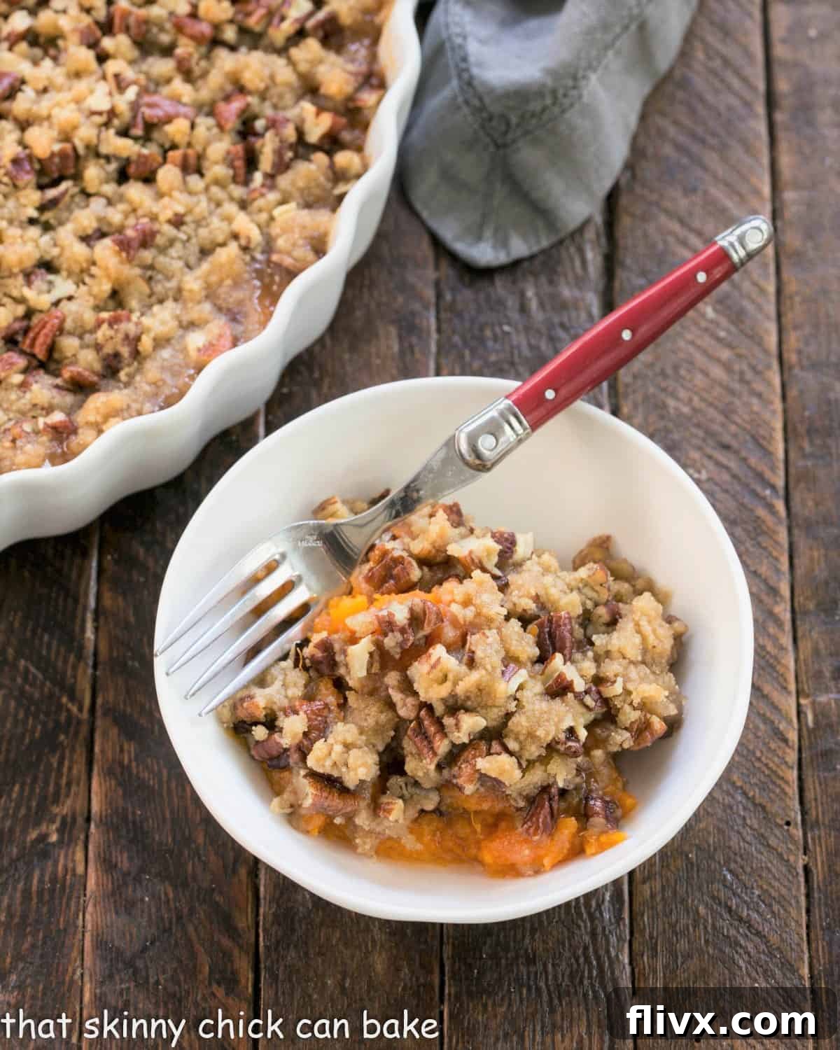 A small white bowl filled with a serving of easy Praline Topped Sweet Potato Casserole, garnished with a red handled fork.
