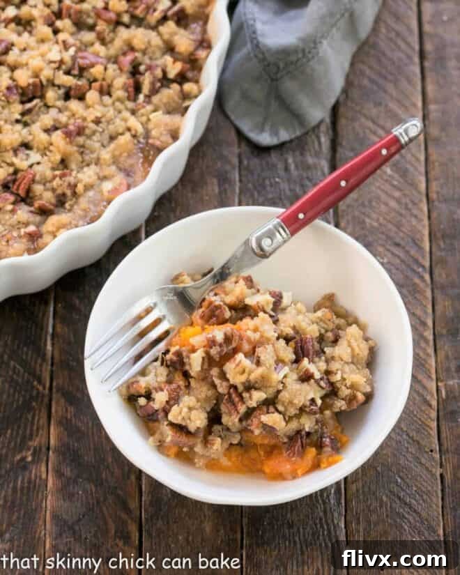 A single serving of sweet potato casserole in a white bowl with a fork, ready to be enjoyed.