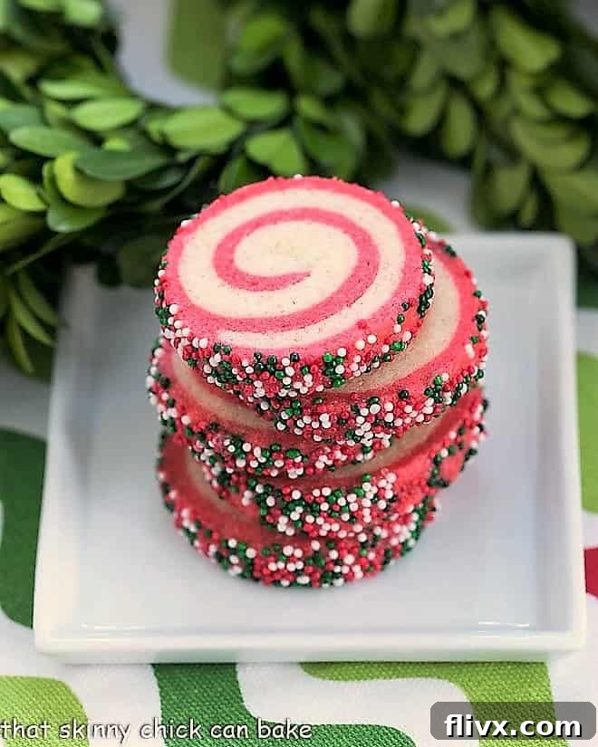 Close-up of baked Holiday Pinwheel Cookies stacked on a square white plate, showing the intricate red and white spirals.