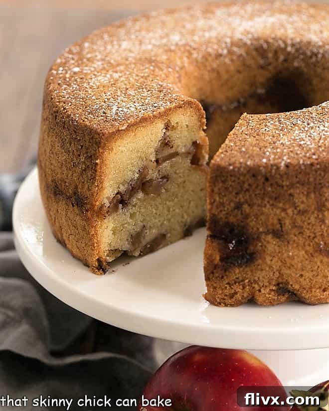 A beautifully baked Cinnamon Apple Bundt Cake, lightly glazed and sitting on a pristine white cake stand, ready to be sliced and served.