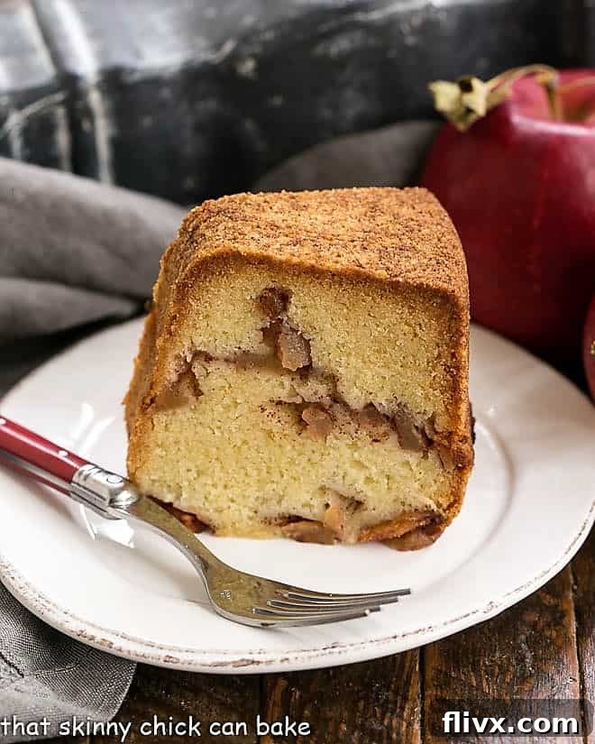 A perfect slice of Cinnamon Apple Bundt Cake resting on a round white plate, accompanied by a fork, showcasing its dense texture and rich apple chunks.