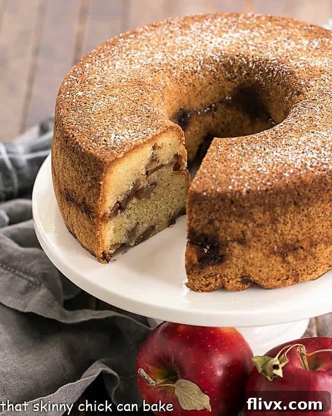 A Cinnamon Apple Bundt Cake on a white cake stand with one slice already removed, highlighting its rich apple filling and moist texture.