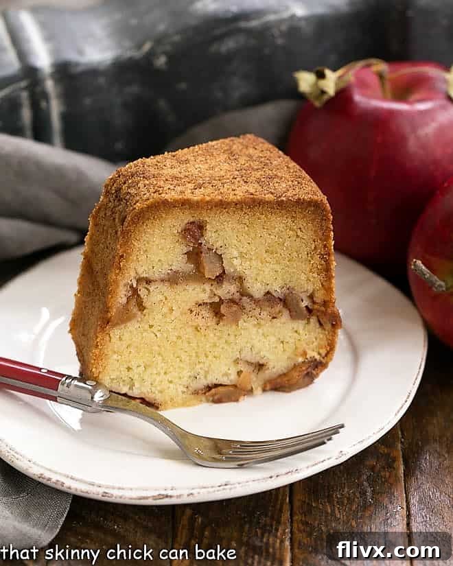 Slice of Cinnamon Apple Bundt Cake on a white plate with a red handled fork, showing the moist cake and apple pieces.