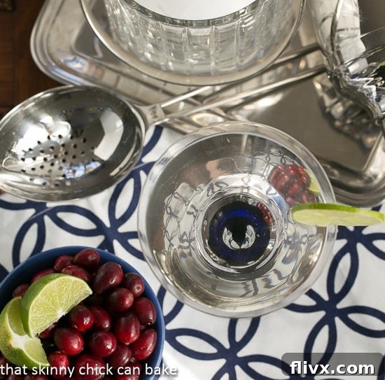 White Cosmopolitans from above with a bowl of garnishes including cranberries and lime.